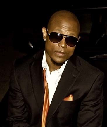 Calvin Richardson sitting on the car while wearing a black shades and black coat