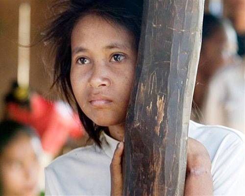 Rochom P’ngieng looking afar while leaning on the wood post and wearing a white blouse