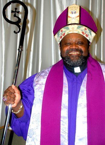 Carl Bean smiling while holding a black cane and wearing multi-colored pontifical vestments.