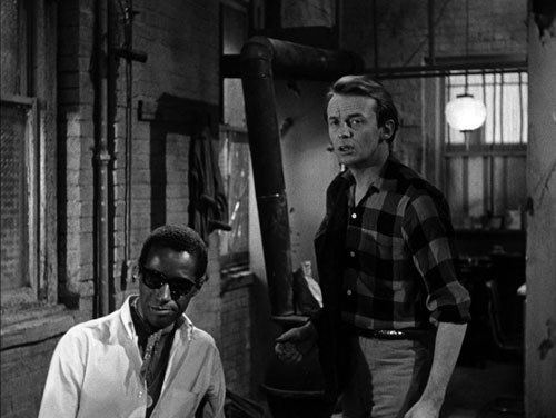 Carl Lee and Warren Finnerty looking at something while Carl is wearing sunglasses, a ribbon scarf, and long sleeves in a scene from the 1961 film, The Connection