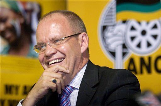 Carl Niehaus laughing while wearing eyeglasses, black coat, striped long sleeves and neck tie