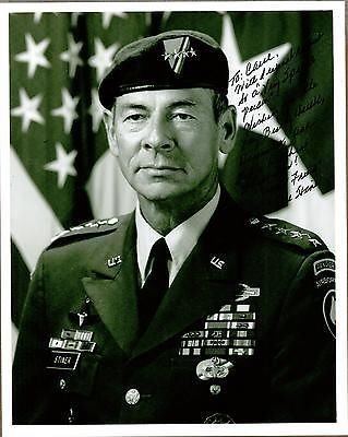 Carl Stiner is serious, a four Star Army General, has faded black hair wearing a US Army Ranger Uniform with four star badge on beret, white top,  black tie, with badges on his chest and broided ranger airborne title on arms.