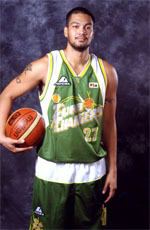 Carlo Sharma is serious, standing in front of a black photo backdrop, holding a basketball (ball) on his waist, has black semi bald hair, tattoo on his right arm, mustache and beard, wearing a number 27 green Turbo Chargers top and bottom jersey.