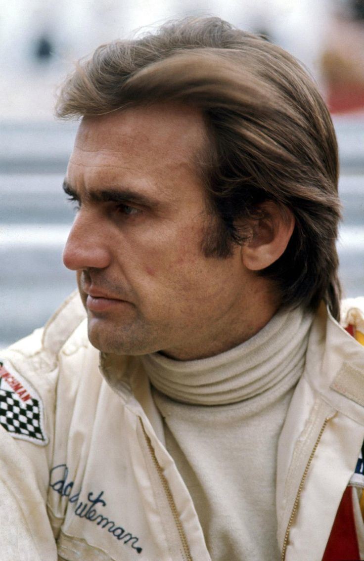 Carlos Reutemann looking afar and wearing a white racing suit