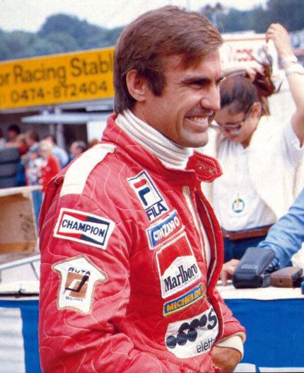 Carlos Reutemann smiling while wearing a red racing suit and white turtle neck long sleeves