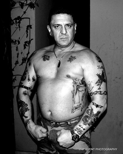 Carlton Leach with a serious face, topless and with tattoos on his body.