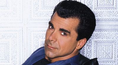 Carman with a tight-lipped smile while wearing a black and blue polo