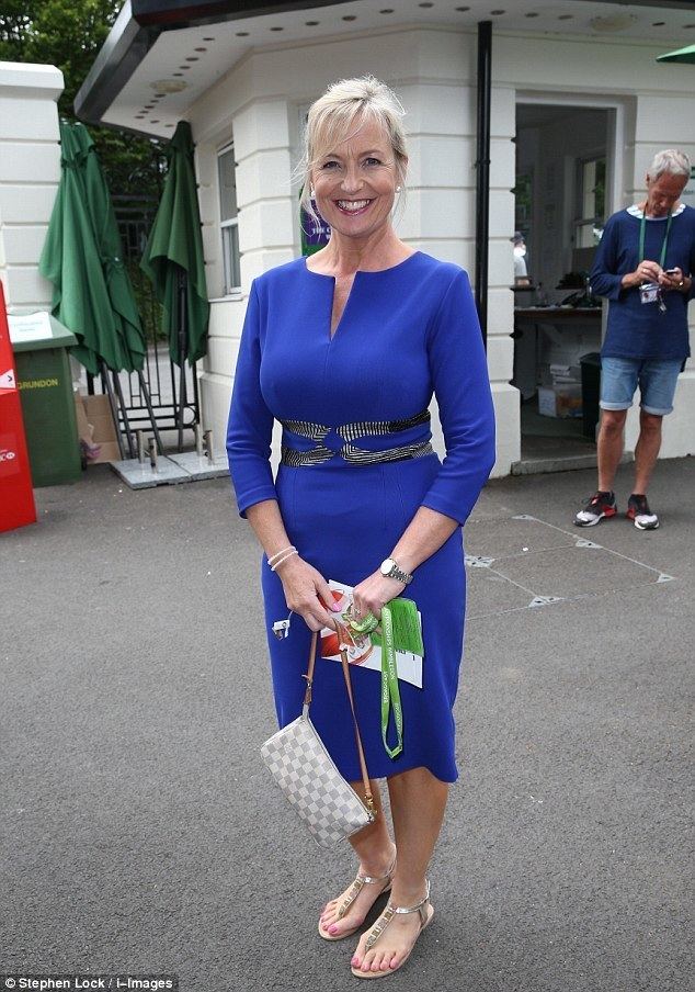 Carol Kirkwood smiling while holding a bag and wearing a blue dress