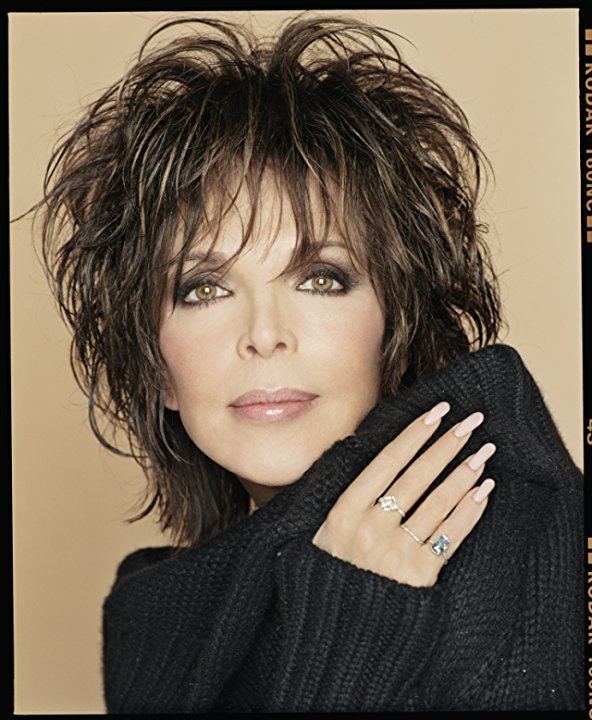 Carole Bayer Sager in her tight-lipped smile and short hair with layers while wearing a black knitted long sleeve blouse and rings