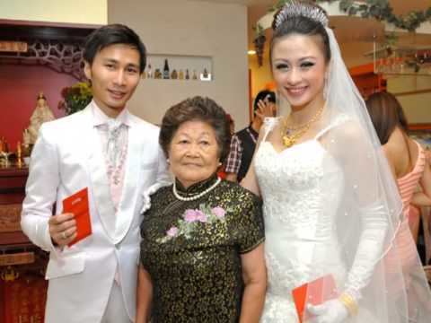 Carrie Lee Sze Kei smiling and wearing a white gown and Stephen Chu also smiling and wearing a white suit on their wedding day together with a woman wearing a green dress.