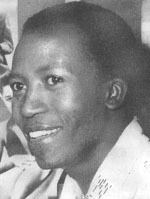 Casey Motsisi smiling and looking on the side while wearing a white blouse