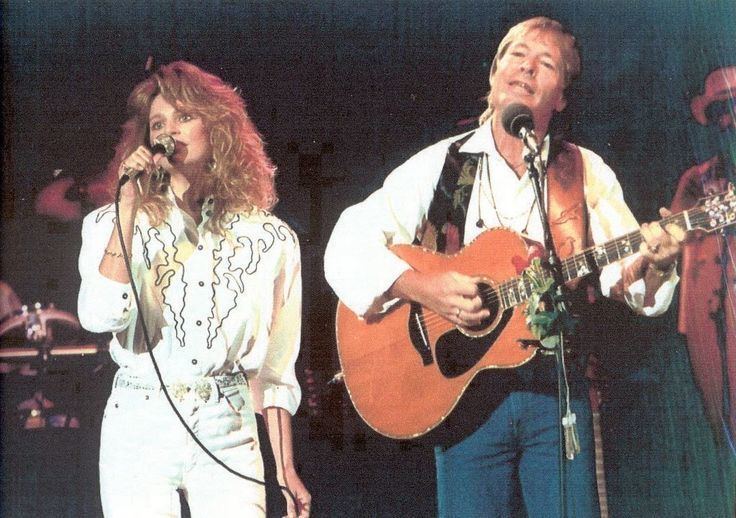 Cassandra Delaney holding a microphone and John Denver playing guitar while singing together