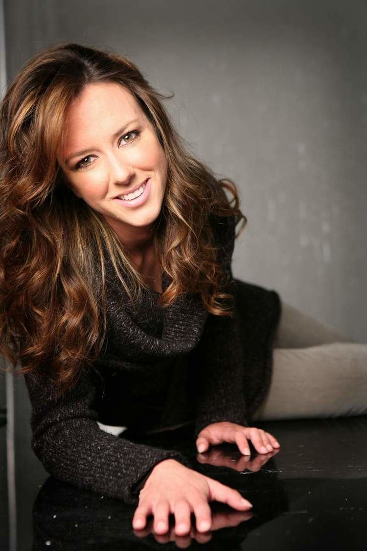 Caterina Guzzanti smiling while crawling on the floor with brown curly hair and wearing a black long sleeve blouse and light gray pants