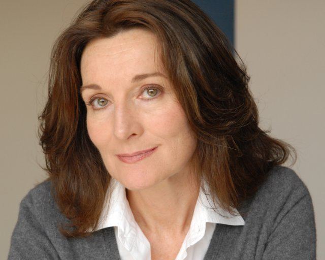 Catherine McGoohan with a tight-lipped smile while wearing a gray blazer and white blouse