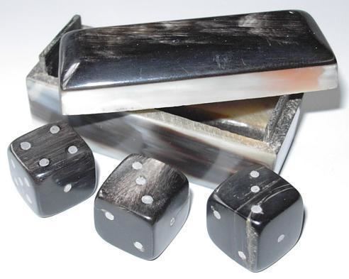 Three black dice made from Zebu horn, with a storage box made of the same material in the background. In the photograph, the dice are showing the values 3, 3, and 4, which gives a point value of 4 (when the dice are rolled, if the outcome is a pair plus another number, the point value is the value of the single die) in the game Cee-lo.