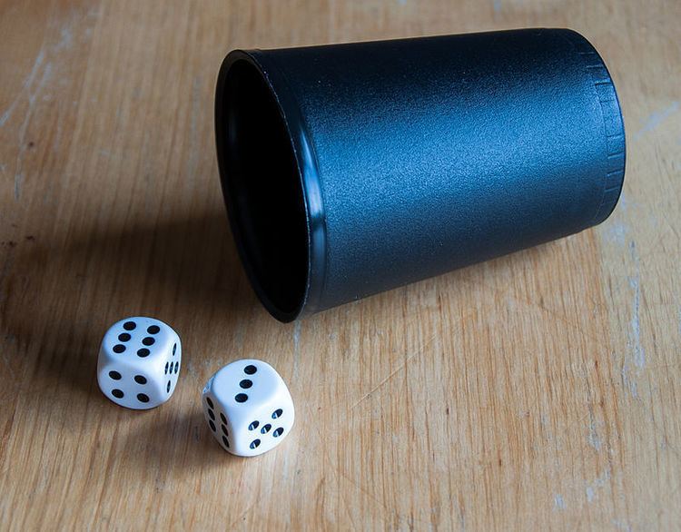 Two six-sided dice and a cup on a wooden surface. In the photograph, the dice are showing the values 6 and 3, which has an odd sum (9). In the game ChÅ-han, players who bet on 'han' (odd) would win their bets.