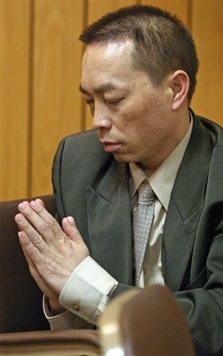 Chai Vang praying at court and wearing a gray suit over a white long-sleeved polo along with a light gray tie.