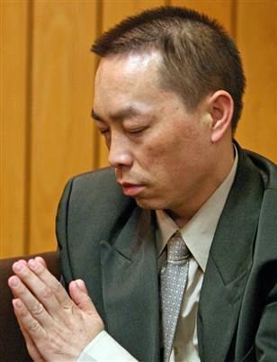 Chai Vang praying at court and wearing a gray suit over a white long-sleeved polo along with a light gray tie.