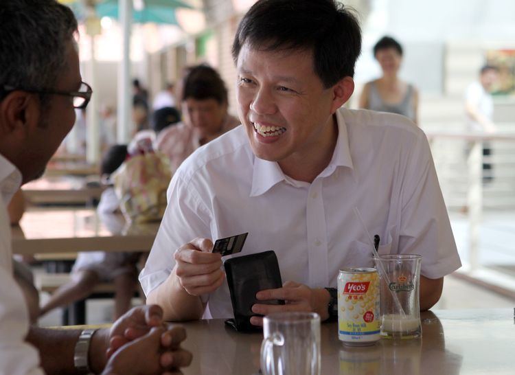 Chan Chun Sing laughing and holding a wallet and card while wearing a white polo