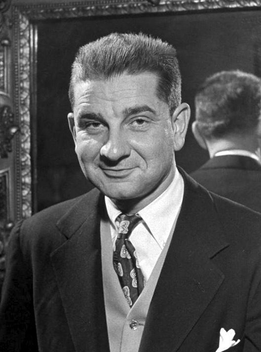 Charles Addams smiling while wearing a coat, vest, long sleeve, and necktie