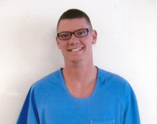 Charles Andrew Williams smiling and wearing blue shirt, eyeglasses and necklace