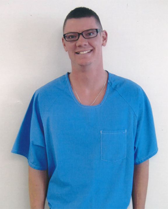 Charles Andrew Williams smiling and wearing blue shirt, eyeglasses and necklace