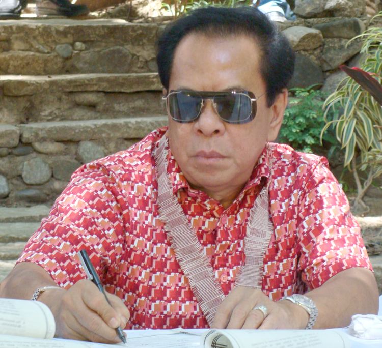 Chavit Singson wearing a red shirt and a pair of sunglasses while writing outdoor