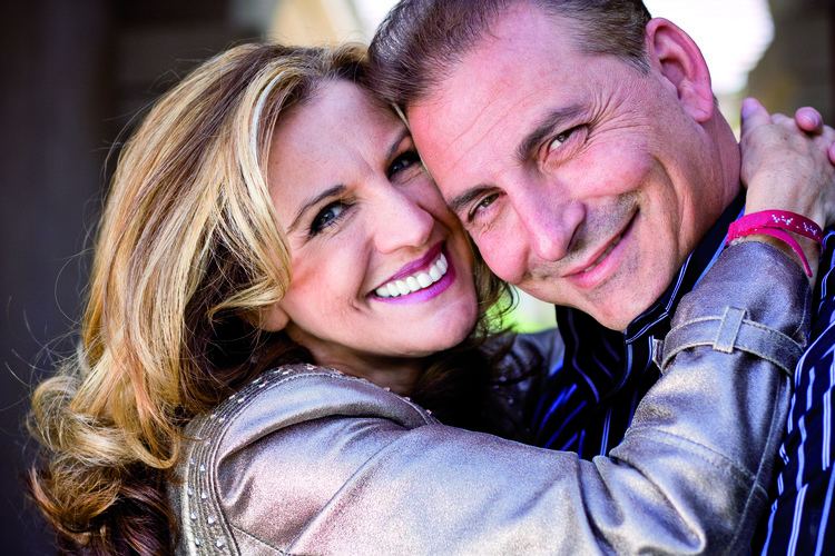 Cheryl Prewitt smiling and hugging her husband Harry Salem II while she is wearing a silver blazer