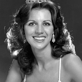 Cheryl Prewitt smiling while wearing a crown, earrings, and sleeveless top