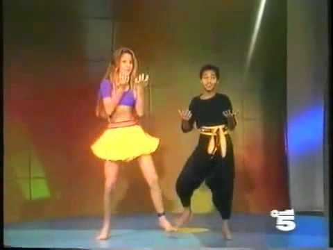 Chico wearing black outfit paired with yellow and red belt & Roberta in her violet top and yellow skirt while dancing Frente A Frente (1989)