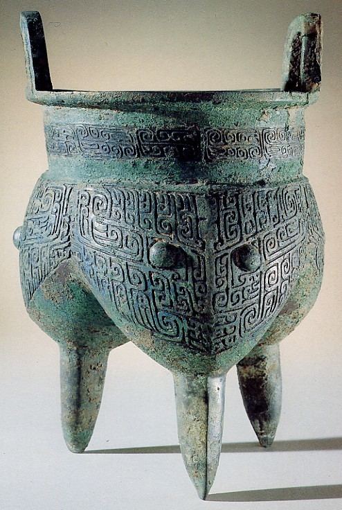 Bronze vessel of the type called li. The vessel has a recessed neck between the three lobes that make up the body ending in short legs, and the everted lip with two round handles.