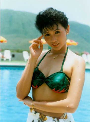 Chingmy Yau smiling while wearing a green swimsuit and a floral wrap skirt