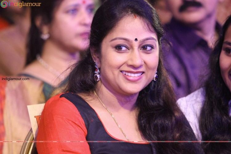 Chippy smiling and looking at something at an event while wearing red and black dress along with a necklace and earrings.