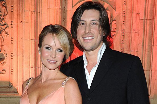 Chris Hughes smiling and wearing a black coat and white long sleeves while Amanda Holden wearing a peach sleeveless dress