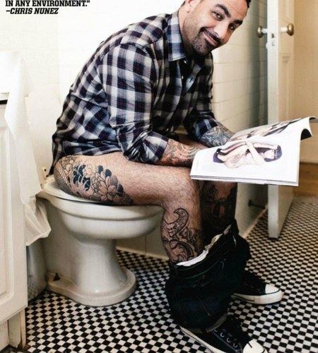 Chris Núñez wearing chekered long sleeves while sitting on a toilet bowl and holding a magazine