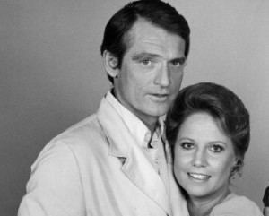 Chris Robinson (left) is serious, has black hair, and wears white long sleeves under a white suit. Leslie Charleson (right) is smiling, has black hair, wearing a white top.