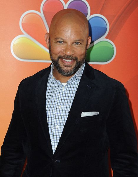 Chris Williams smiling with thicker facial hair and wearing black coat and checkered shirt underneath in an event.