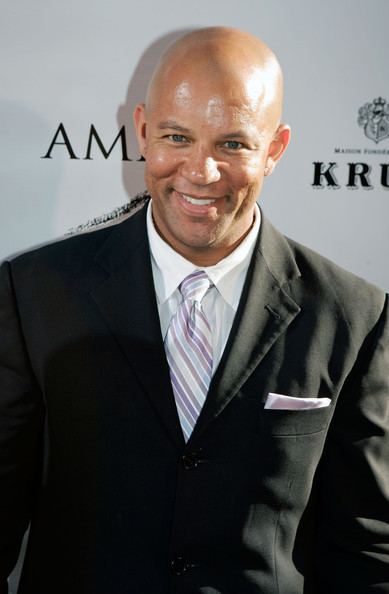 Chris Williams with no facial hair smiling and wearing black coat with white buttoned shirt and light pink tie.