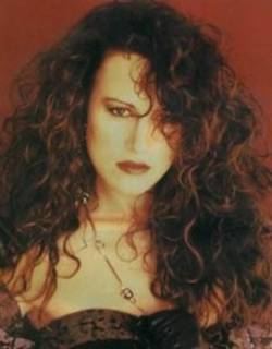In a red background, Chrissy Steele is serious, has long curly hair wearing a necklace and a dark brown dress.