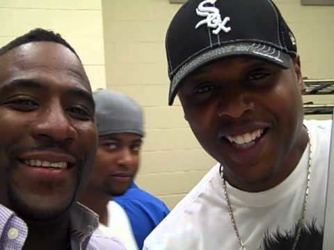 Christian Payton smiling while wearing a black cap, necklace, and white t-shirt, and the man beside him wearing violet long sleeves