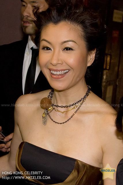 Christine Ng with a big smile, wearing a necklace and a brown tube dress.