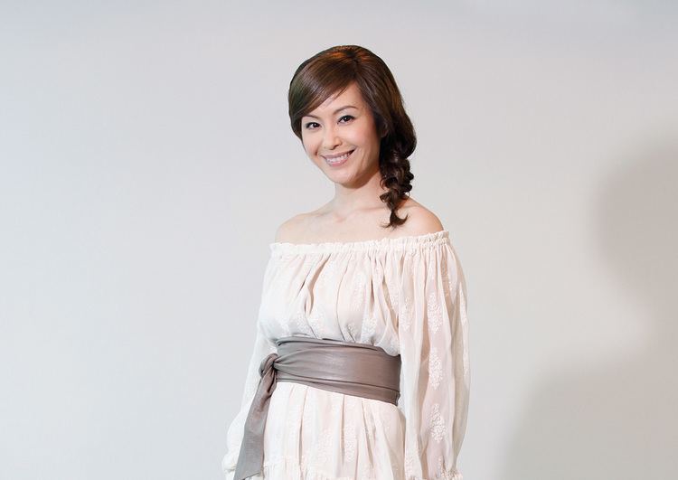 Christine Ng smiling and wearing a white dress with a cloth belt.