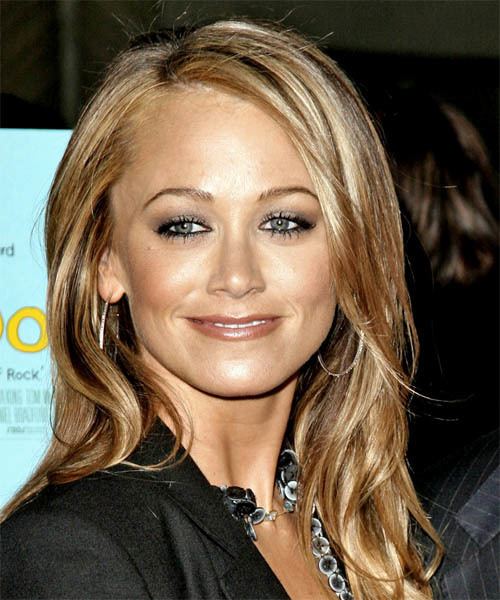 Christine Taylor smiling with blonde wavy hair while wearing hoop earrings and a black blouse with buttons