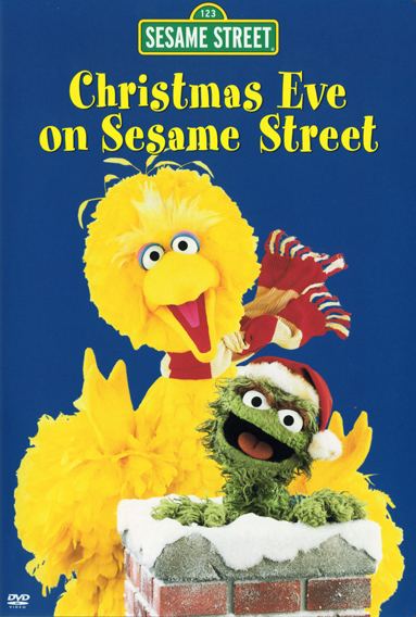 The cover of the Christmas Eve on Sesame Street, has blue background, at the top is the title of the show Sesame Street in a green street sign, with “Christmas Eve on Sesame Street in yellow font below” at the bottom from left Big bird is happy, beak wide open hands up standing, has yellow feathers, wearing a red and white scarf, at the right Oscar the Grouch is happy standing inside a red brick chimney with snow on top, has olive green body and a brown eyebrows, wearing a red christmas hat.