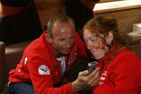 Christophe Saioni smiling and listening to a recorder with her wife, Mruša Ferk Saioni and both wearing a red jacket