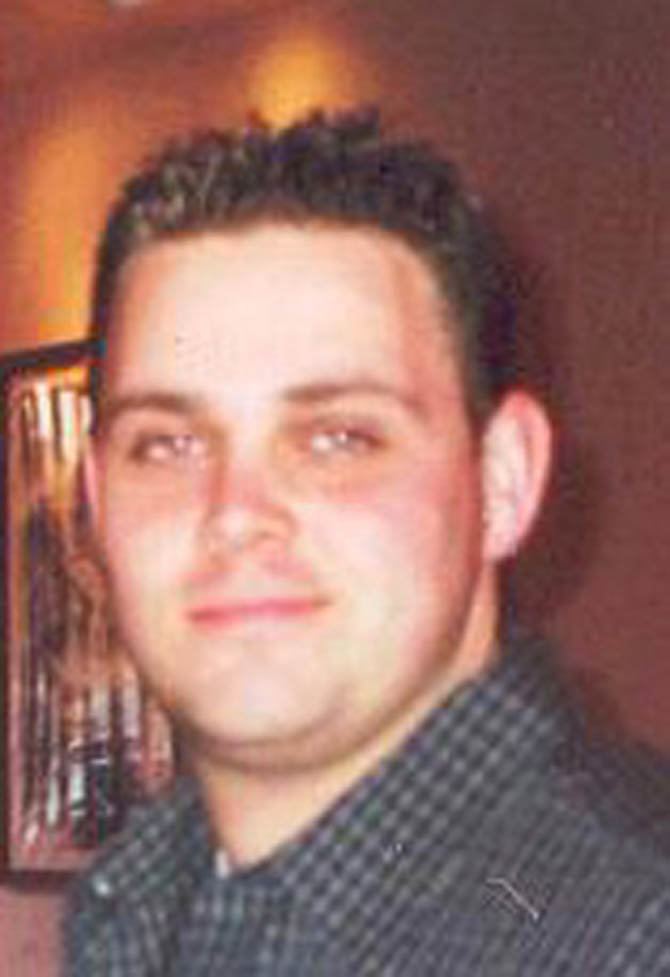 Christopher Amoroso smiling, with curly hair, and wearing a black checkered polo shirt.