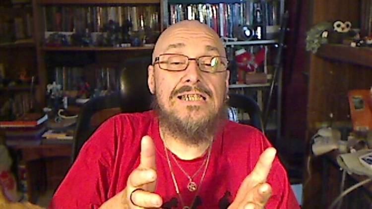Christopher Thomas Knight wearing eyeglasses and a red shirt while talking.