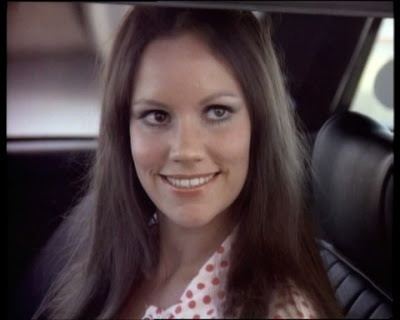 Christy Hartburg smiling and wearing a polka dot shirt inside a car.
