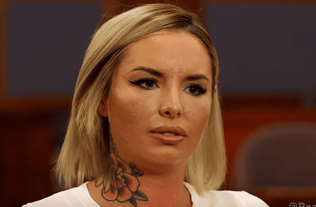 Christy Mack looking at something with a serious face, a tattoo on her neck, and a blonde shoulder-length hair while wearing a white blouse