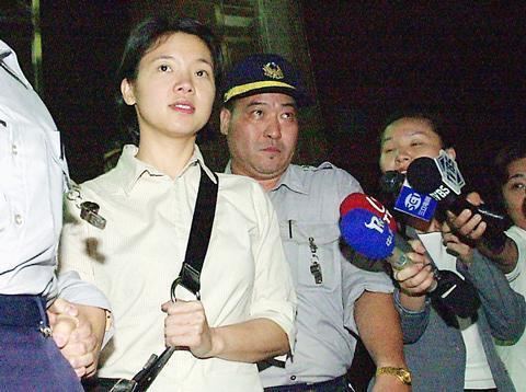 Chu Mei-feng with a serious face while surrounded by police officers and reporters. Chu Mei-feng is wearing a black sling bag and an off-white polo shirt.